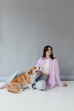 Neşeli bir kadın, neşeli Corgisiyle güzel, parlak bir stüdyo odasında güzel vakit geçiriyor.
