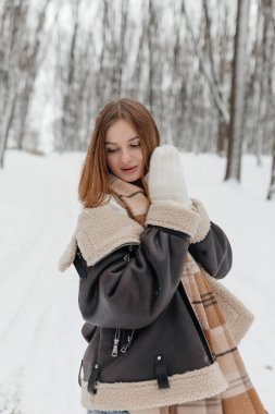 Sıcak bir kış kıyafeti giymiş bir kadın, etrafındaki karlı ormanın büyüleyici güzelliğini neşeyle kucaklıyor.