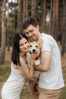 Huzurlu ve güzel bir ormanda, neşeli bir çift neşeli ve hayat dolu Corgilerini kucaklıyor, doğanın canlı güzelliği arasında gerçek bir aşk anını yakalıyor.