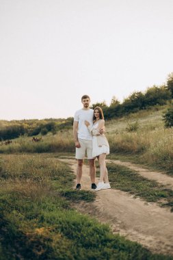 Güneşli, canlı bir arazide, sevgi dolu bir çift, doğanın yemyeşil ve dingin güzelliği arasında güzel, samimi bir yakınlık anını yakalar.