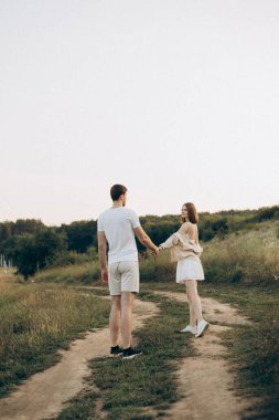 Genç bir çift, canlı doğayla çevrili güzel bir yolda romantik ve hoş bir yürüyüş yapar.