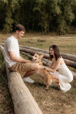 Neşeli bir çift, sevimli köpekleriyle neşeli bir şekilde oynuyorlar sakin bir açık hava ortamında, bereketli doğayla çevrili.