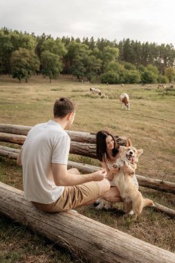 Neşeli bir çift, canlı bir çayırda ağaçlarla çevrili köpekleriyle neşeyle meşgul olan bir kütükte oturur ve basit zevklerden zevk alırlar.