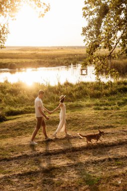 Gün batımında sakin bir gölün kenarında köpekleriyle yürüyüş yapan bir çiftin romantik sahnesi.