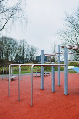 Açık havada güvenli bir kauçuk yüzey üzerinde dinlenen çelik oyun alanı ekipmanlarını gösteren manzaralı bir manzara.