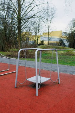 Yalnız bir salıncak, doğanın güzelliğiyle sarılmış canlı kırmızı bir yüzeyde sessizce oturur.