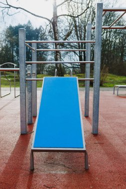 Canlı, mavi bir slayt güzel bir parkta, yemyeşil ağaçlar ve çeşitli oyun alanlarıyla çevrili.