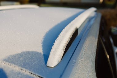 Donmuş arabanın çatısının detaylı bir yakın çekimi yumuşak güneş ışığında parıldayan karmaşık buz kristalleri sergiliyor.