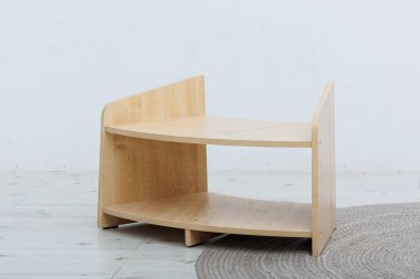 İnce malzemelerden yapılmış sağlam bir ahşap raf, el değmemiş beyaz bir duvarın önünde, yumuşak, dokulu bir halının üzerinde zarif bir şekilde duruyor.