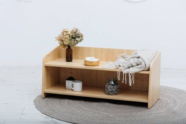 Güzel işlenmiş ahşap bir raf rahat bir battaniyeyle süslenmiş ve üzerinde taze çiçekler bulunan büyüleyici bir vazo.