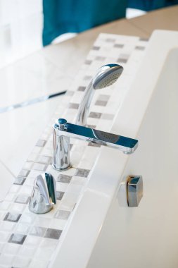 Banyo dekorunda hem tasarım hem de işlevsellik gösteren duş başlığı takılı bir küvetin yakın görüntüsü.