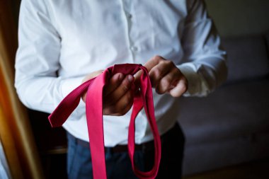 Gıcır gıcır beyaz gömlek giyen bir adam, boynuna canlı kırmızı bir kravat bağlıyor ve mükemmel düğüm formasyonuna odaklanıyor.