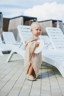 Havuz başı atmosferinin eğlencesine dalmış tapılası bir bebek, güneşli bir günde saf neşe ve masumiyeti somutlaştıran yumuşak bir havluya sarılır.
