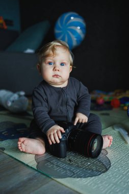 Sevimli bir bebek küçük bir kamerayla neşe içinde oynuyor, çocukluk merakının ve yaratıcılığın sevimli özelliklerini renkli oyuncaklarla dolu samimi bir ortamda sergiliyor.