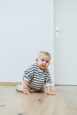 Neşeli bir bebek parlak ahşap bir zeminde sürünüyor, aydınlık, sıcak bir yaşam alanında, keşfetmek için rahat ve güvenli hisseden eğlenceli bir merak gösteriyor.