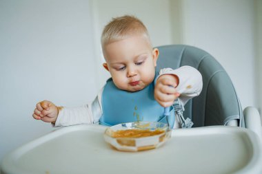 Yüksek sandalyedeki neşeli bir bebek, çocukluğunun ilk zamanlarındaki yemek vaktinin eğlencesini ve karmaşasını yansıtarak, keyifli aile anları yaratıyor.