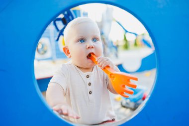 Parlak mavi gözlü bir bebek neşeli turuncu bir oyuncakla neşeli, renkli bir oyun parkında oynar ve güler. Neşeli mavi bir çember ya da arka plan tarafından mükemmel çerçevelenir.