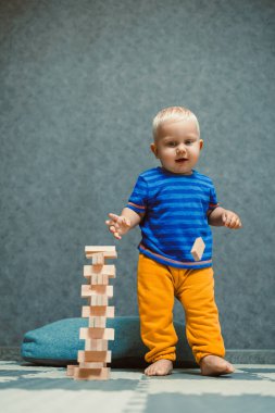 Neşeli ve neşeli bir çocuk renkli ve canlı bir blok kulesinin yanında gururla durur, yaratıcı oyun ve sınırsız yaratıcılıkla edinilen önemli becerileri gözler önüne serer.