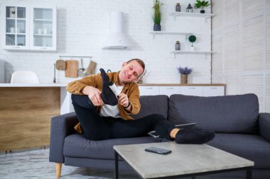 Genç bir adam şık bir kanepede rahatlar, şık spor ayakkabısını mükemmel bir uyum için ayarlar. Odaların modern dekorasyonu uzun bir günün ardından gevşemek için sıcak bir atmosfer yaratıyor.