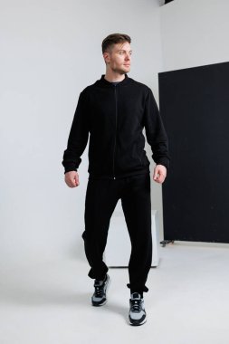 Bir adam kendine güveni tam siyah bir ceket giyer. Aynı siyah pantolona sahip. Modern moda anlayışı ve zarafetini sergiler.