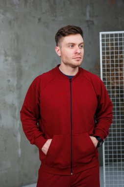 İki eli de ceketinin cebine saklanmış parlak kırmızı bir ceket giyen bir adam rahat bir hava yayıyor.