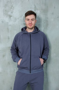 Bir adam ellerini cebine sokup rahat bir şekilde görünüşünü tamamlayan şık bir kapüşon giyer.