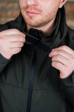 Sakallı bir adam şu anda ceketinin fermuarını rüzgarlık kumaşından ayarlıyor.