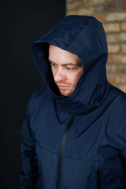Bir adam, modern ve modaya uygun görünümlü, uygun bir kapüşonlu, şık bir mavi ceket giyiyor.