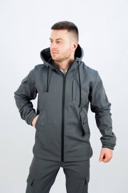 Düzgün kesilmiş sakallı bir adam, ekstra sıcaklık ve koruma için işlevsel bir başlık içeren şık gri bir ceket giyiyor.