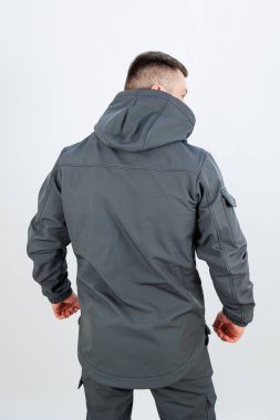 Manzara, üzerinde fonksiyonel bir kapüşonu olan şık gri bir ceket giyen bir adamın arkasını yakalıyor.