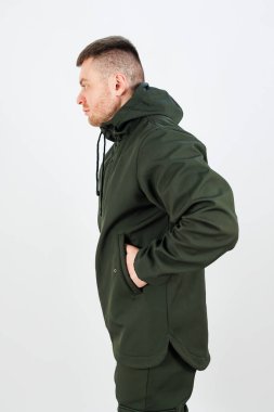 Canlı yeşil bir ceket giyen bir adamın iki eli de ceketinin cebinde rahatça saklıdır.