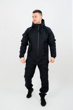 Bir adam saf beyaz bir arka planda duruyor, şık bir siyah ceket giyiyor ve tarzını tamamlayan bir pantolon giyiyor.