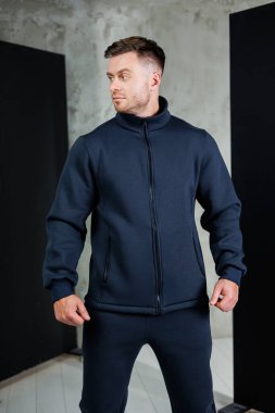 Sakallı bir adam şık mavi bir ceket ve uyumlu bir pantolon giyiyor. Kıyafetinin içinde oldukça şık ve şık görünüyor.