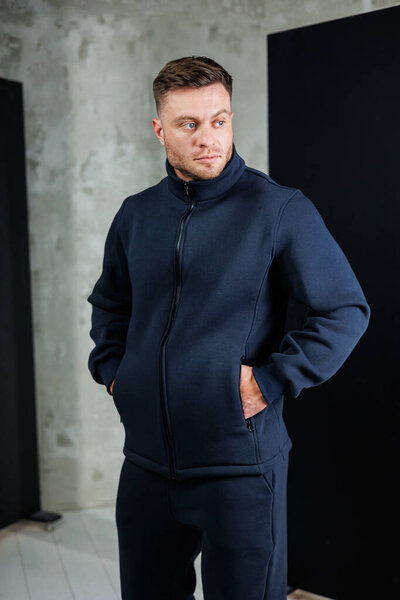 A man is standing confidently while wearing a blue jacket and matching pants, with both of his hands comfortably tucked into his pockets