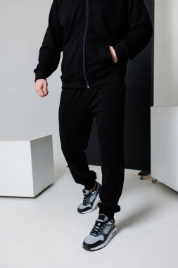 Bir adam siyah bir ceket giyiyor ve takım elbisesinin bir parçası olarak siyah eşofman giyiyor.