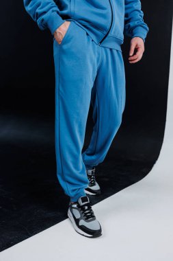 Bir adam rahat mavi eşofman ve şık siyah beyaz spor ayakkabılar giyerken görülüyor.