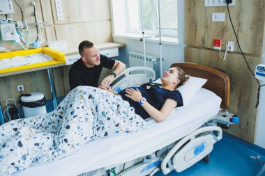 Doğum sırasında acı çeken bir kadın. Hamilelik, doğum konsepti. Çocuk doğururken hamile kadının elini tutan şefkatli bir adam. Destekleyici erkek, doğum sırasında genç kadına yardım ediyor..