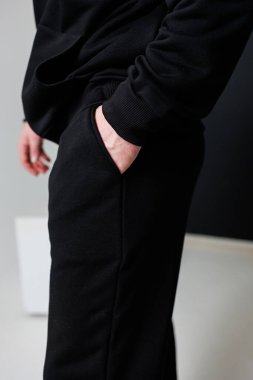 Siyah eşofman giymiş bir adam, tek eliyle pantolonunun cebine sıkışmış, rahat bir hava katıyor.