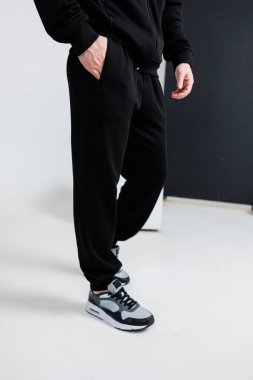 Gri spor ayakkabılarla eşleştirilmiş siyah eşofmanlı bir adam iki elini rahatça cebine sokuyor.