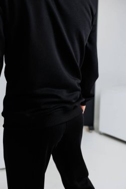 Tarz sahibi siyah gömlekli ve parlak siyah pantolonlu bir kişinin arka planı şık bir tek renkli görünüm yaratıyor.