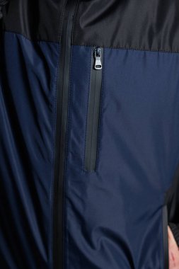 İşte size kapüşonlu ve rüzgarlığı andıran zarif mavi bir ceketin fermuarını gösteren detaylı bir yakın çekim resmi.