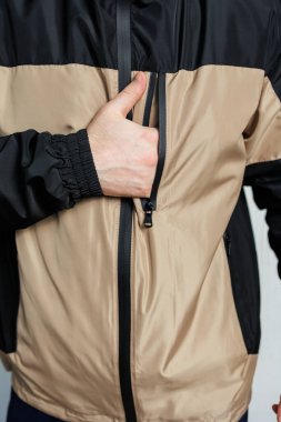 Havalı, siyah ve bronz bir ceket giymiş bir adam elini dış giysisinin ceplerinden birinin içine sokuyor.