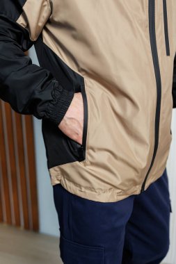 Bronz tenli ve siyah ceketli bir adam elini cebine sokmuş, rahat ve rahat bir tavır takınıyor.