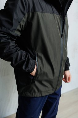 Şık, siyah ve yeşil ceketli bir adam elini ceketinin cebine sokmuş olarak görülebilir.