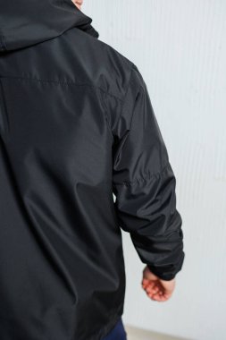 Bir adam kapüşonlu siyah bir ceket giyiyor. Yağmur ya da rüzgar gibi elementlere karşı mükemmel bir koruma sağlıyor.