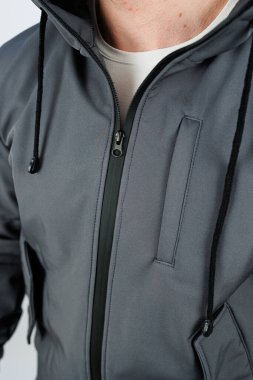 Bir adam şık gri bir kapüşon giyerken görülüyor. Parlak siyah bir fermuarı var. Modern ve modaya uygun bir görünüm sergiliyor.