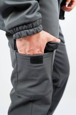 Şık, gri bir ceket giymiş bir adam, rahat bir şekilde elleri cebinde duruyor ve kıyafetlerini gösteriyor.