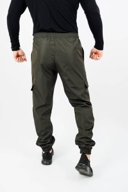 Siyah gömlek ve yeşil kargo pantolon giyen, tarzını ve kıyafet seçimini sergileyen bir adamın dikiz aynasından bakınca kendine güvenen bir tavır sergiliyor.