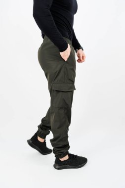 Kargo pantolonu ve parlak siyah ayakkabılar giyen bir adamın elleri rahat bir şekilde cebine sokulur.
