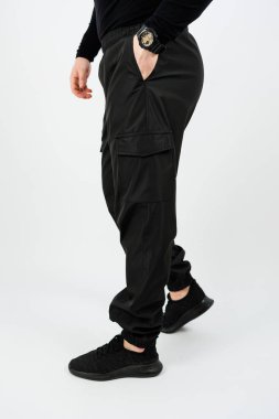 Siyah pantolonlu ve siyah ayakkabılı bir adamın iki eli de rahat bir şekilde kıyafetlerinin cebine yerleştirilmiştir.